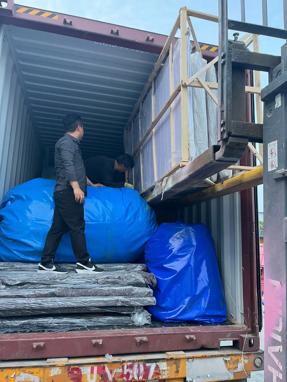 Loading a 40-foot container: platform sections and crates bottom, long poles and fascia racks upright along the walls.